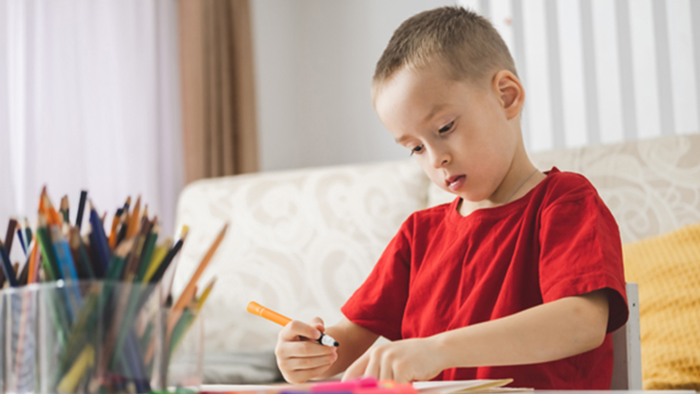 A pre-school aged boy draws with markers in an office with a couch.